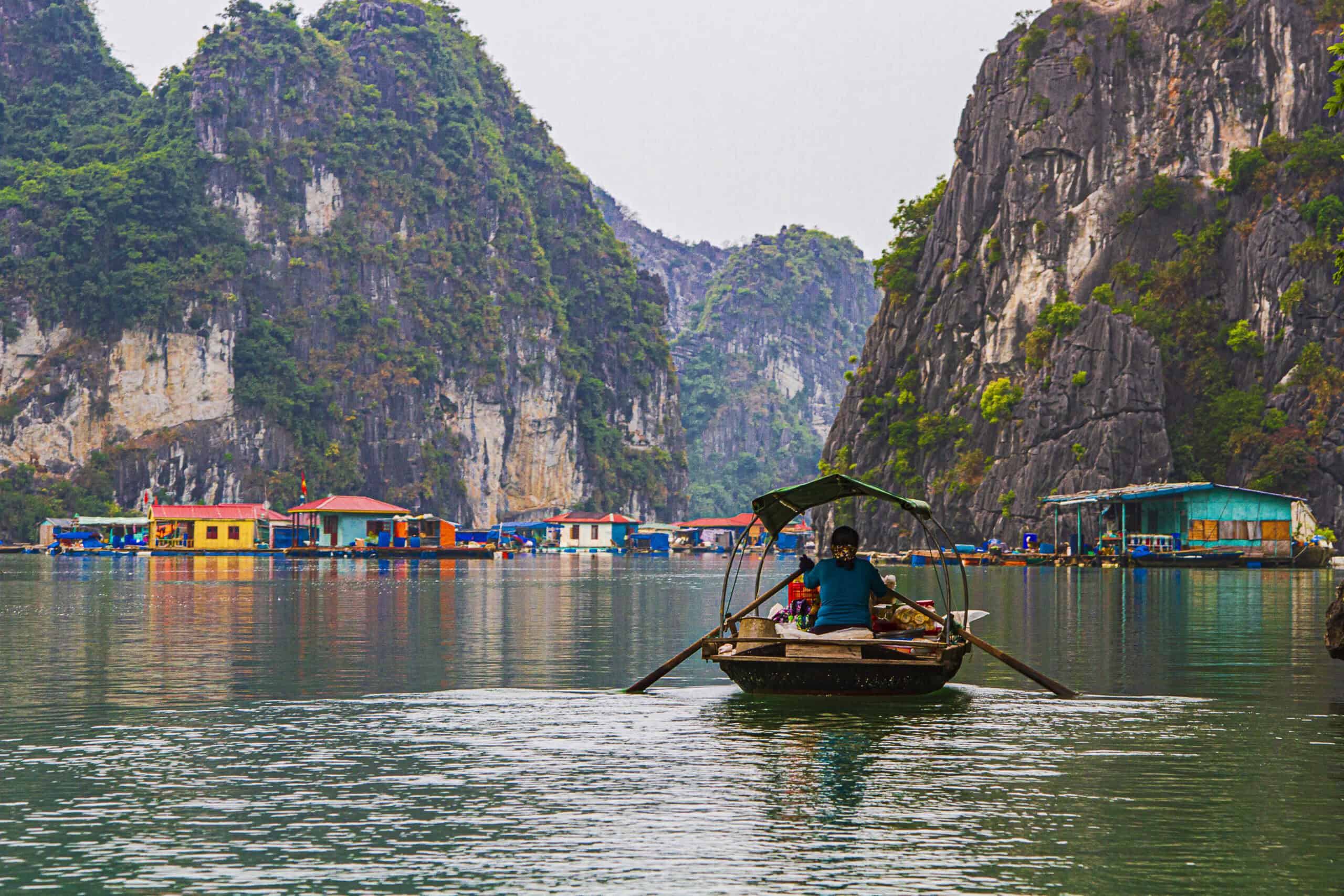 The image shows a fishing village in the famous Ha Long Bay surrounded by towering limestone islands which protect it from storms